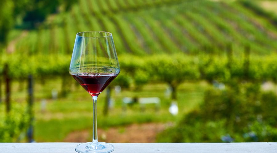 Must-visit wineries in California Glass of red wine and vineyards.